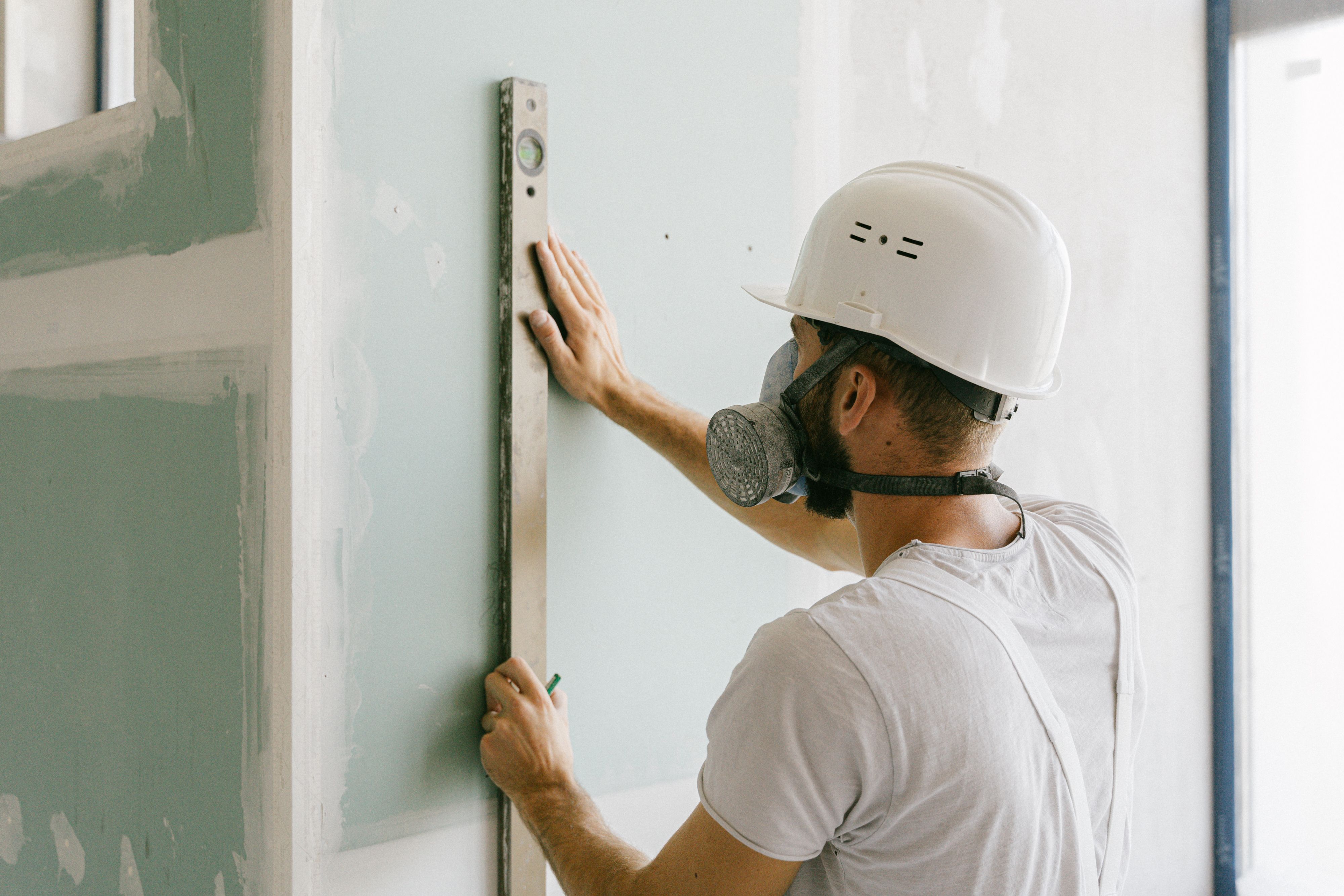 Bouwvakker met helm en stofmasker meet een wand op.
